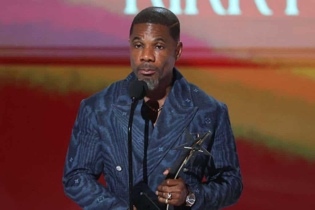 Kirk Franklin holding an award at a ceremony, speaking into a microphone.